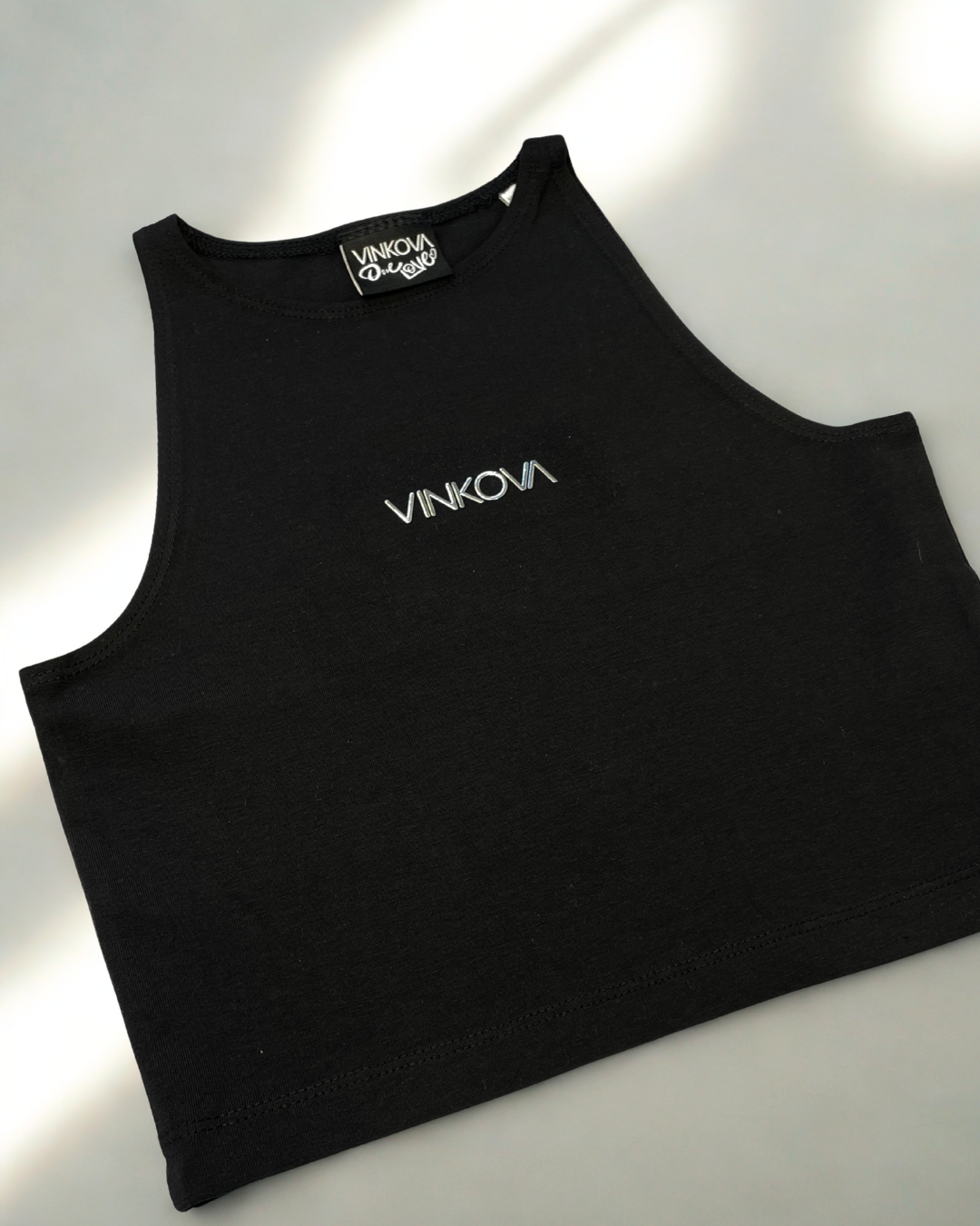 Top halter nero Vinkova, dettaglio del collo alto e del logo sul petto.