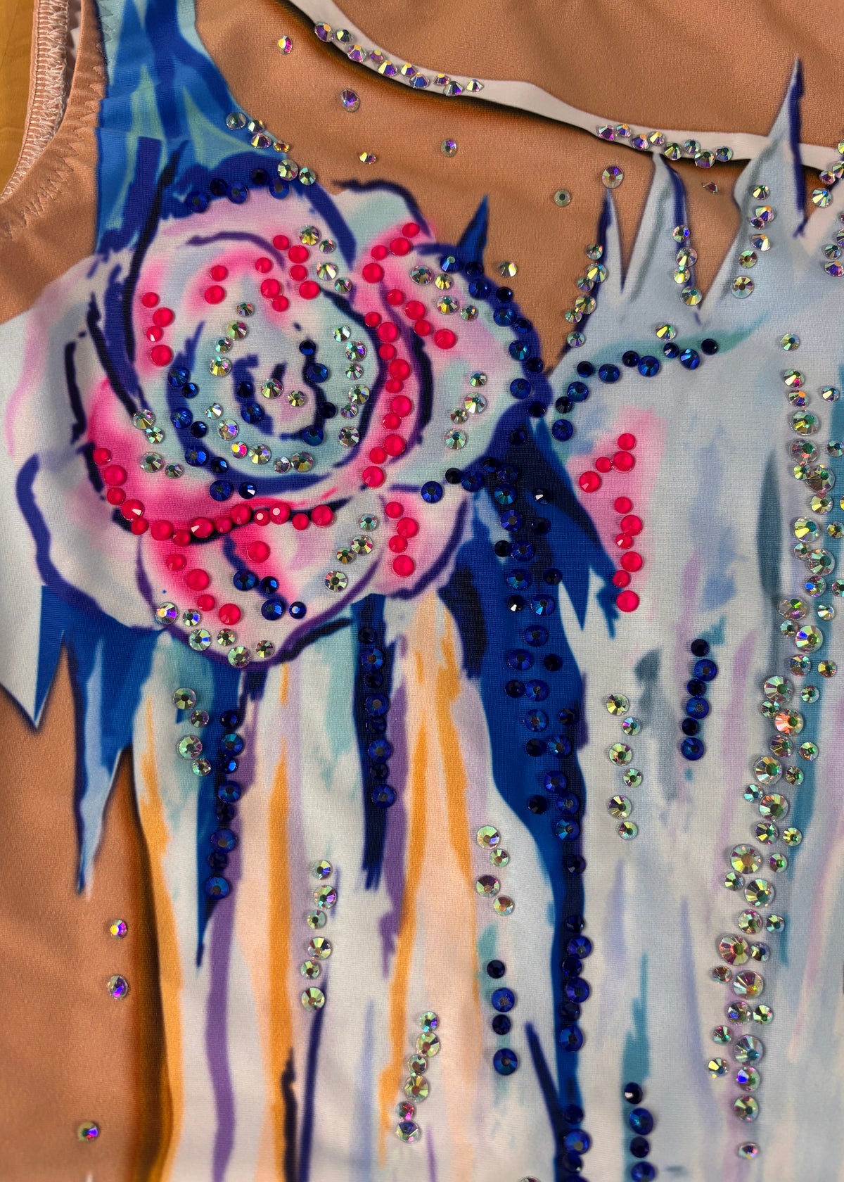 Dettaglio del fiore rosa e blu e degli ornamenti blu, rosa e iridescenti vicino allo scollo.