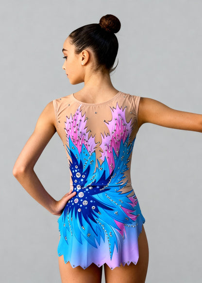 Maillot de gimnasia rítmica sin mangas en degradados de azul y rosa sobre base nude. Incluye un diseño de plumas estilizadas y detalles de pedrería plateada que crean un efecto dinámico y elegante en el cuerpo.